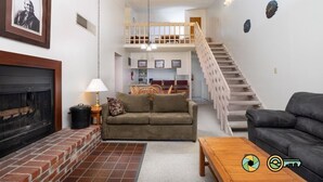 Una sala de estar con chimenea, un sofá, una mesa de centro y una escalera que sube a un nivel superior.