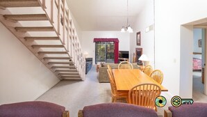 Amplia sala de estar con una mesa de comedor de madera, sillas, un sofá y una escalera.