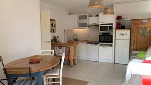 Een kleine keuken met witte kastjes, een houten eettafel en een rode bank.