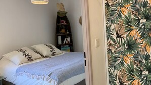 Een slaapkamer met een bed, een hanglamp, een boekenkast en een muur met een tropisch bladpatroon.