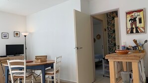 Een eetgedeelte met een tafel en stoelen, een televisie, en een keuken met een waterkoker en keukengerei.
