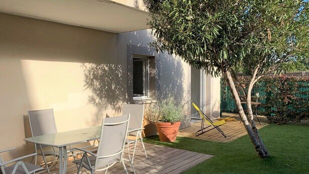Een terras met een tafel en stoelen, een bloempot en een kleine boom.