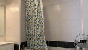 Een badkamer met een douchegordijn met een cactustextuur, een witte badkuip en een metalen droogrek met een fles zeep.