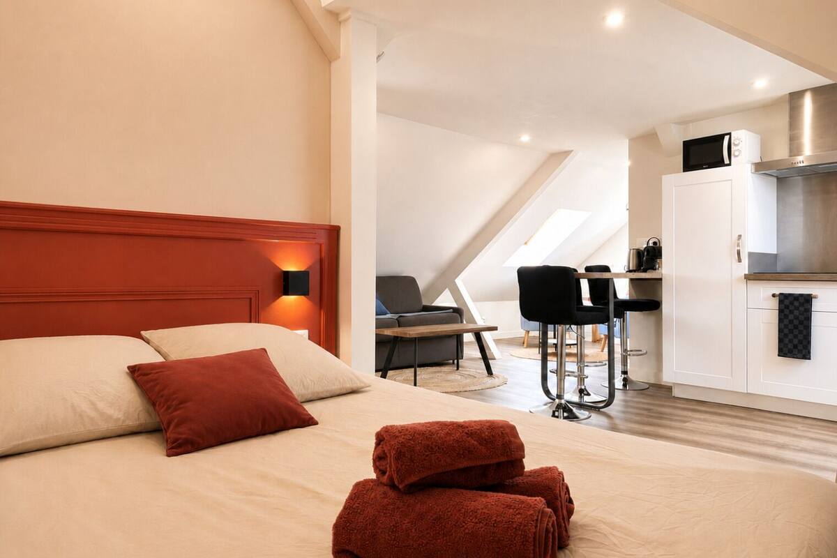 Habitación de hotel con cama, escritorio, silla, kitchenette y luz en el techo.