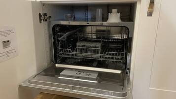 An open dishwasher with a control panel, a glass of water, and a bottle on the top shelf.