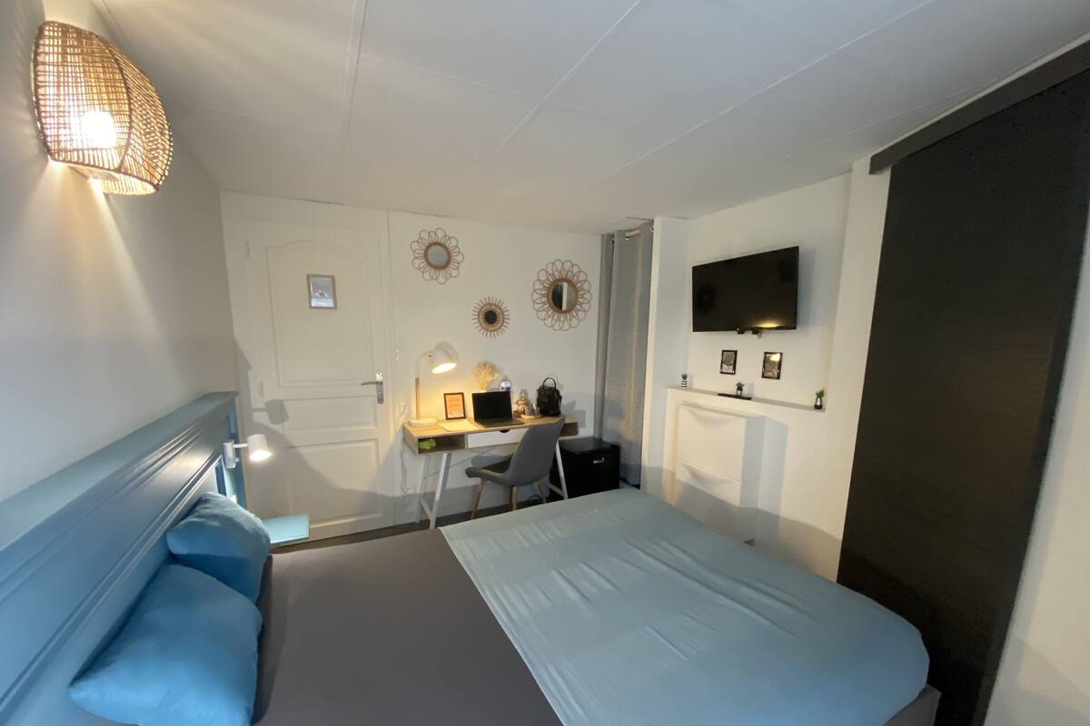 Un dormitorio con cama, escritorio, silla y televisor en la pared.