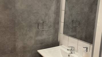Un baño con lavamanos blanco, un espejo y una ducha.