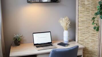 Un'area lavoro con un laptop, una piccola pianta in vaso, un vaso con fiori secchi e una sveglia appesa al muro.