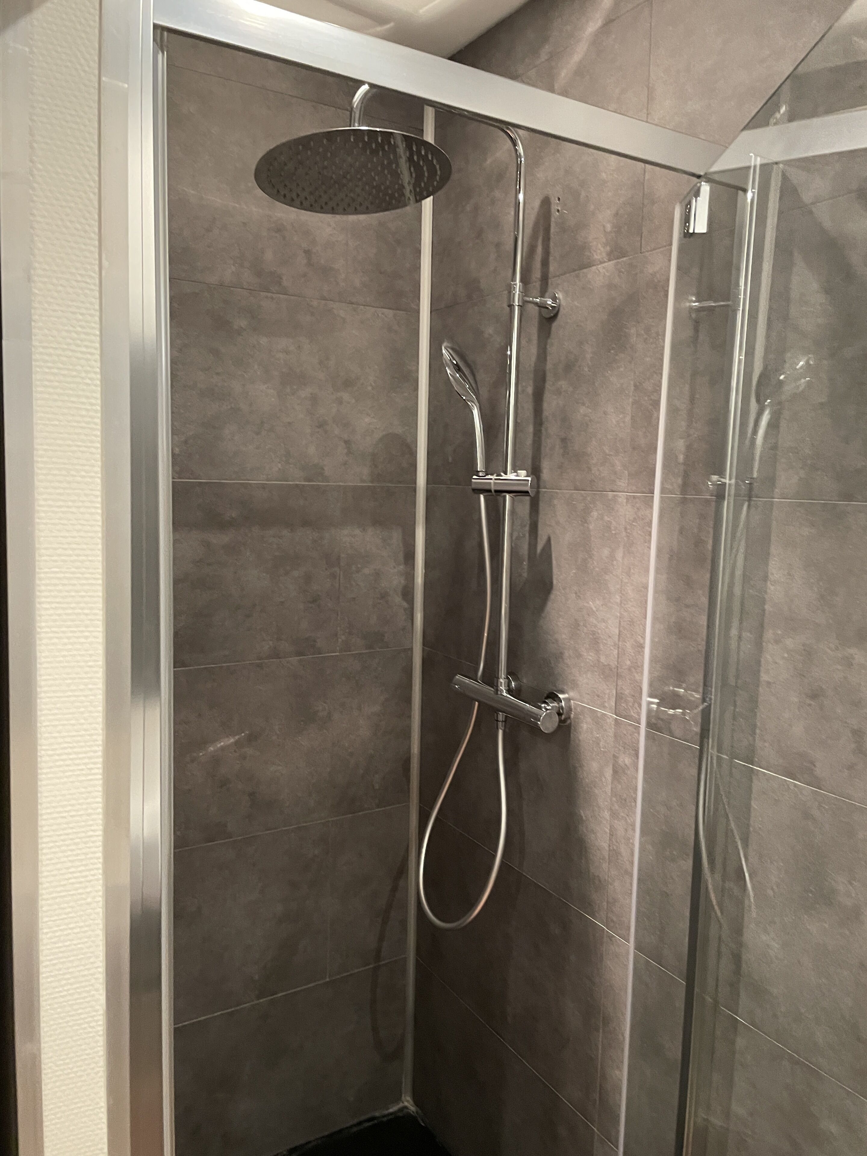 A walk-in shower with a handheld showerhead, a wall-mounted faucet, and a handheld showerhead.