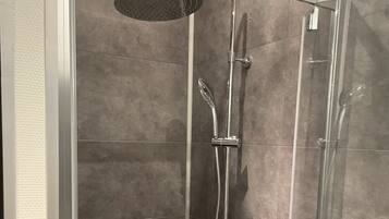 A walk-in shower with a handheld showerhead, a wall-mounted faucet, and a handheld showerhead.