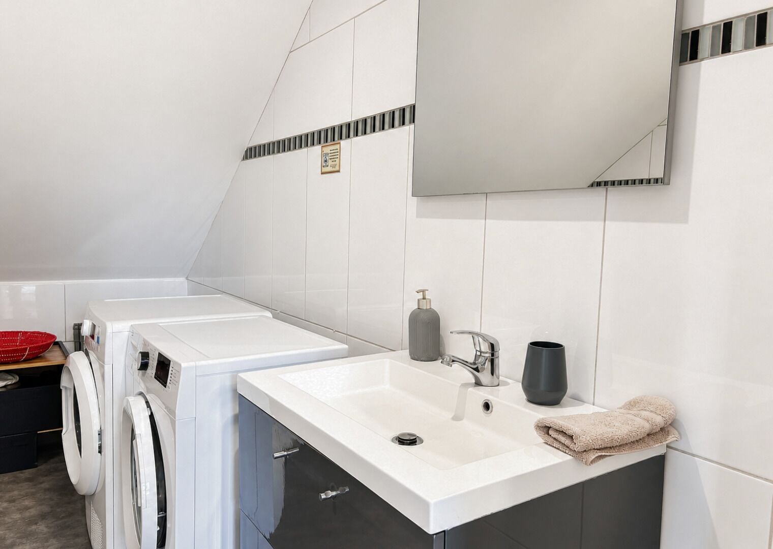 A modern bathroom with a white sink, a mirror, a towel, and a washing machine.