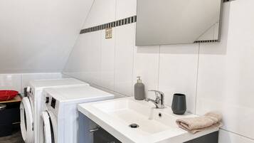 A modern bathroom with a white sink, a mirror, a towel, and a washing machine.