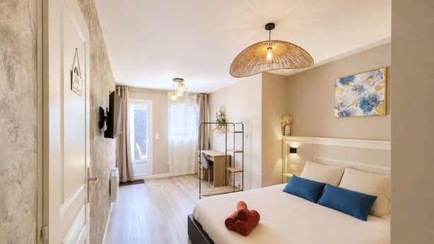 Een hotelkamer met een bed, bureau, stoel, hanglamp en een schilderij aan de muur.