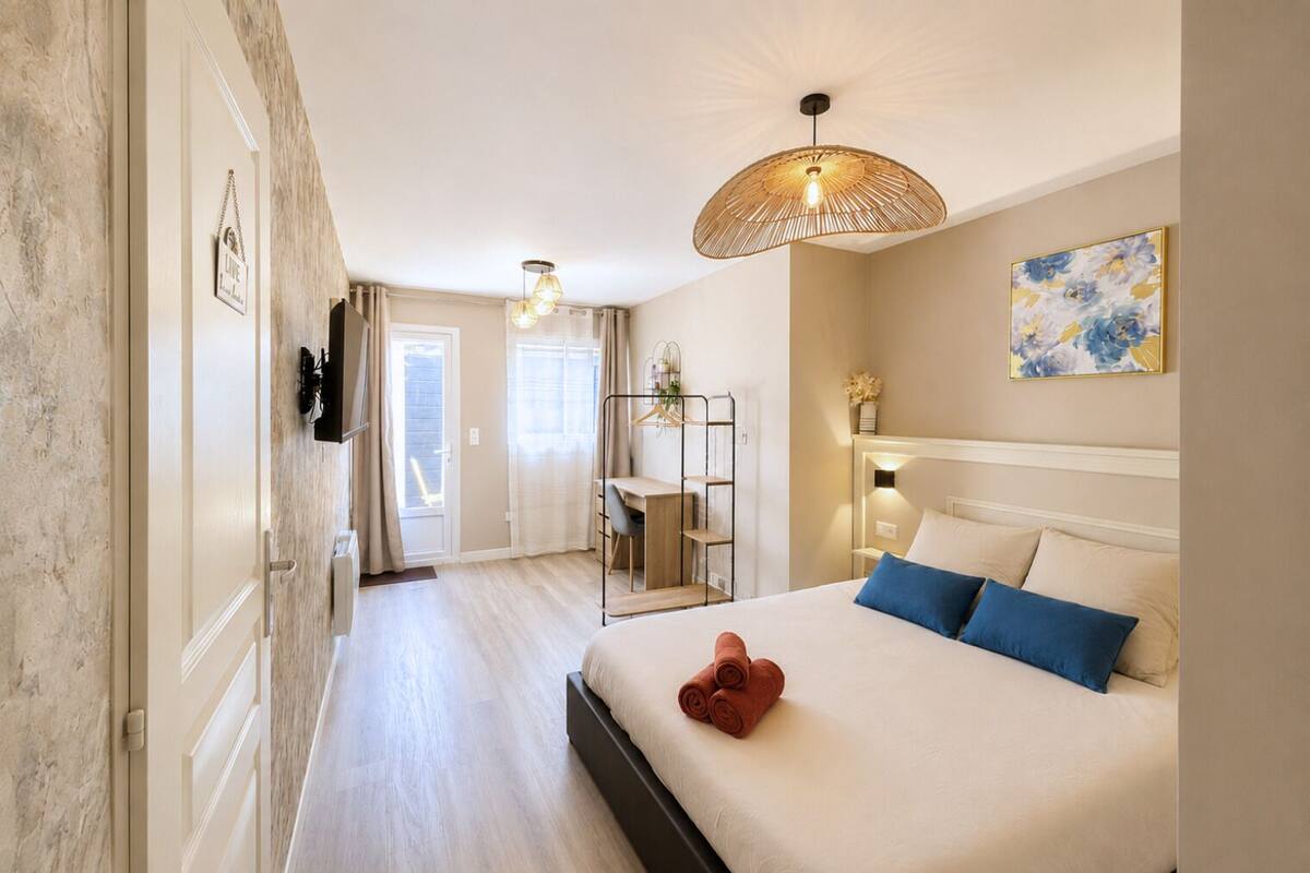 Habitación de hotel con cama, escritorio, silla, lámpara colgante y un cuadro en la pared.
