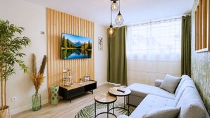 Een moderne woonkamer met een grote flatscreen televisie, een houten accentmuur, een bank, een salontafel en een potplant.