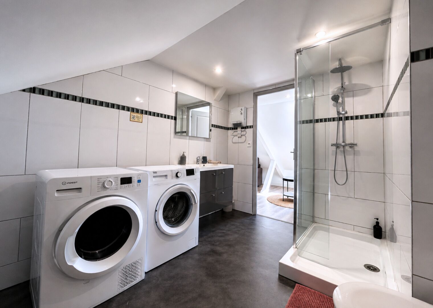 A modern bathroom with a washing machine, a shower, and a sink.