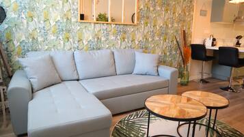 A modern living room with a light grey sectional sofa, two round wooden tables, and a large mirror on the wall.