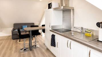 Una cocina moderna con armarios blancos, electrodomésticos de acero inoxidable y un comedor con sofá gris y sillas negras.