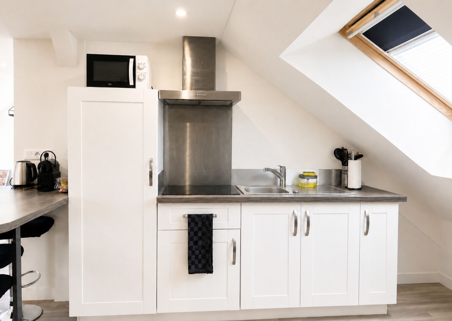 A modern kitchen with white cabinetry, a stainless steel range hood, a microwave, and a skylight.