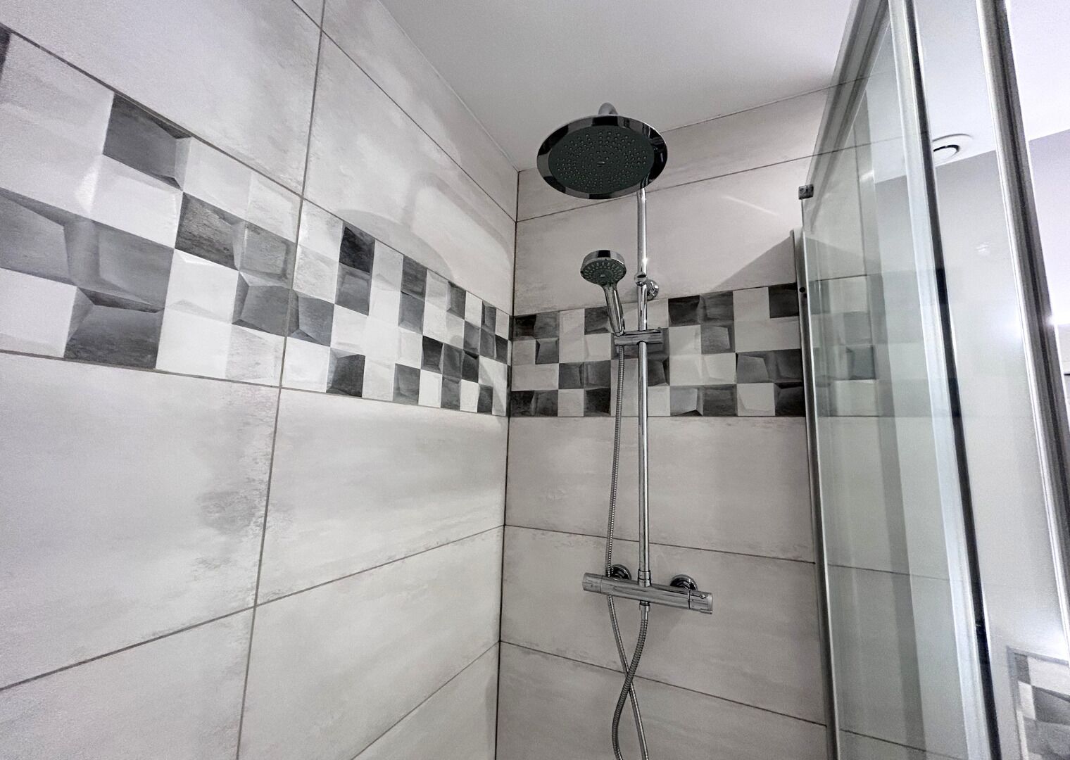 A shower with a round head, a handheld showerhead, and a wall-mounted control panel.