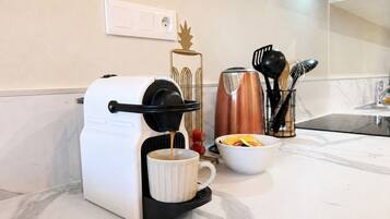 A coffee maker on a kitchen counter with a coffee mug, a bowl of sugar packets, and a coffee pot in the background.