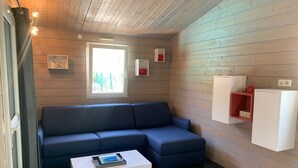 Una habitación moderna con un sofá azul oscuro, una mesa de centro blanca y una ventana con vistas a zonas verdes. Hay armarios empotrados y un estante con un objeto rojo.