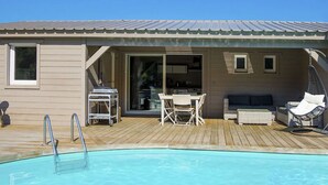 Un área de piscina con una terraza de madera, piscina, mesa con sillas y un sofá.