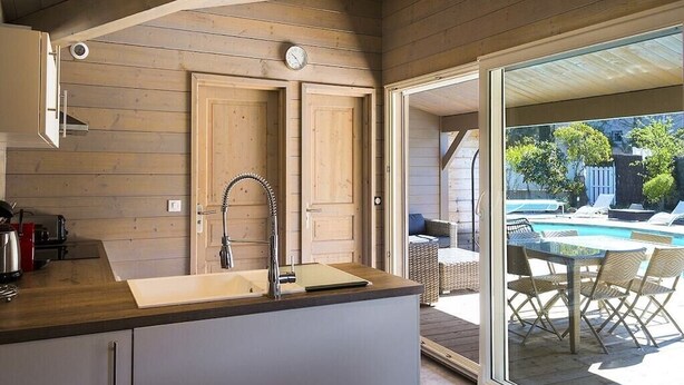 Una cocina con paredes de madera, un lavamanos y una ventana con vista a una zona de piscina.