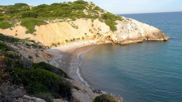 Un paisaje costero con una playa de arena, acantilados rocosos y vegetación.