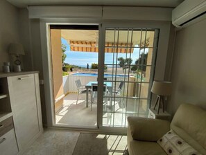 A compact room with a sliding glass door leading to a balcony with a pool and outdoor furniture.