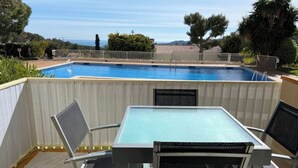 Una piscina al aire libre con vistas al mar, rodeada por una valla de madera y equipada con una mesa y sillas.