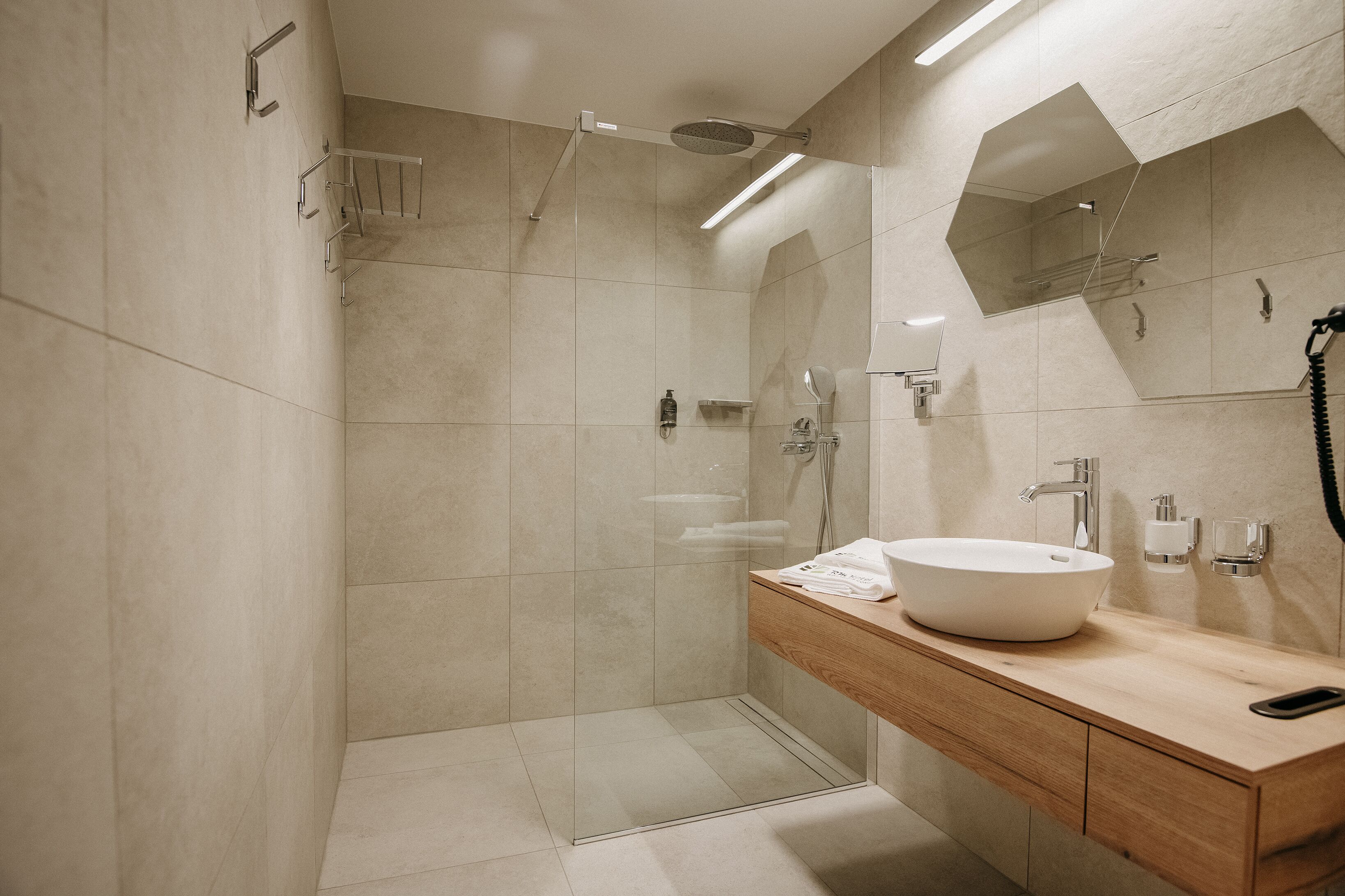 A modern bathroom with a glass-enclosed shower, a wooden vanity with a white sink, and a large mirror above the sink.