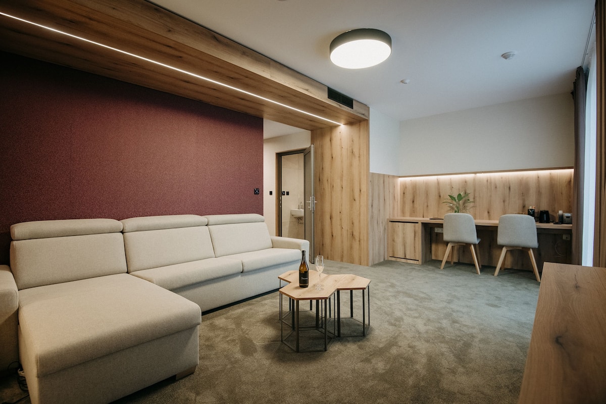 Una sala de estar moderna con un sofá seccional, una mesita de madera con una botella y un vaso, y un escritorio con dos sillas.