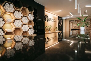 A hotel reception area with a modern design, featuring a wooden hexagonal display of towels, a reception desk, and a potted plant. - RM Hotel wellness & congress (Prievidza)