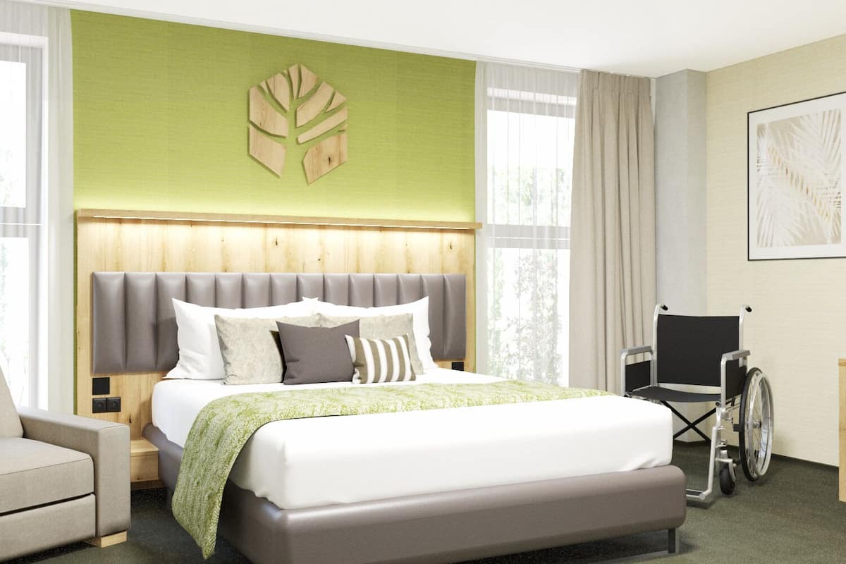 Habitación de hotel con cama, una silla, una silla de ruedas y una pared de acento verde.