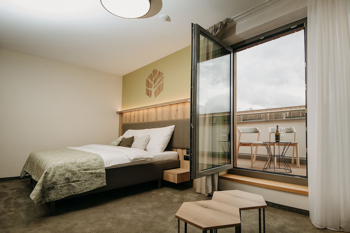 Habitación de hotel con cama, una mesita y un gran ventanal con vistas a la ciudad.