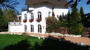Ein weißes, zweistöckiges Haus mit geneigtem Dach und zahlreichen Fenstern, verbunden durch einen Kiesweg, der zur Eingangstür führt.