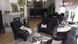Ein Wohnzimmer mit Kamin, zwei schwarzen Ledersofas, einem Glastisch und einer Kristallleuchter.