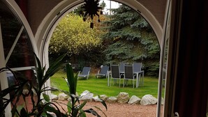 Une pièce dotée d’une grande fenêtre en arc d’où l’on peut admirer un jardin agrémenté de chaises et d’une table.