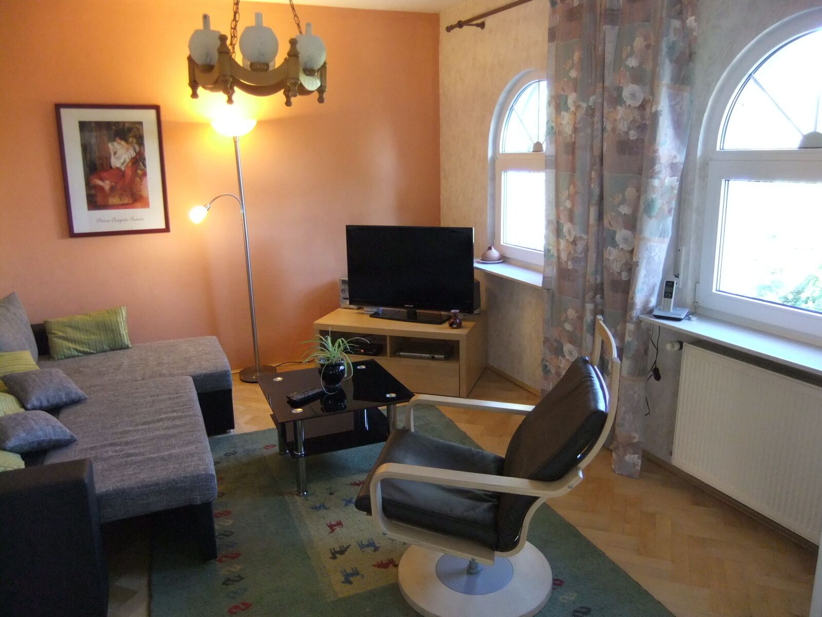 Un soggiorno con divano, poltrona, televisore, lampada e finestra con tende.