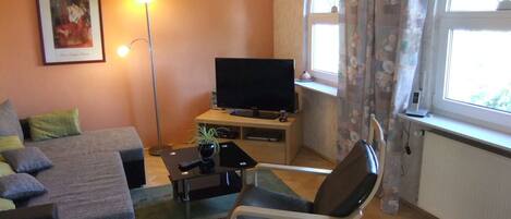 Un soggiorno con divano, poltrona, televisore, lampada e finestra con tende.