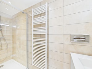 Een moderne badkamer met een douchecabine van glas, een witte handdoekhouder en een wastafel met een chromen kraan.