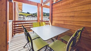 A wooden interior with a table and chairs, a view of a mountainous landscape, and a wooden ceiling structure. - Luxurious 2-Bedroom Apartment in New Residence, Sleeps 6 – Heart of Les Gets (Les Gets)