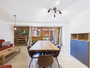 A modern dining area with a wooden table, black chairs, and a television on the wall.
