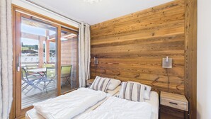 A bedroom with a large bed, a wooden wall, a sliding glass door leading to an outdoor area, and a small bedside table. - Luxurious 2-Bedroom Apartment in New Residence, Sleeps 6 – Heart of Les Gets (Les Gets)
