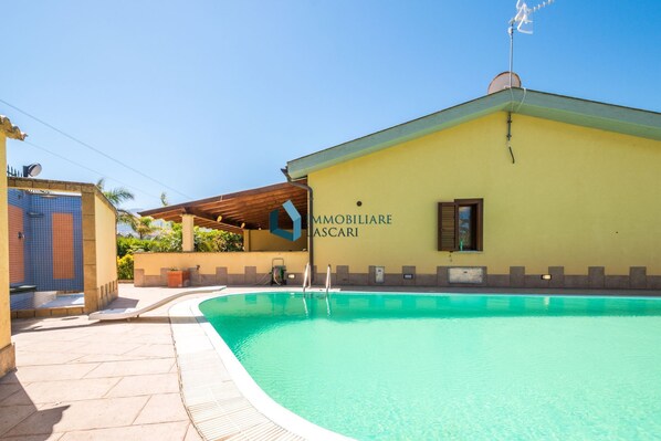 A building with a swimming pool, a covered outdoor area, and a sign reading 'IMMOBILIARE LASCARI'.