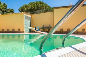 A swimming pool with a diving board, a lounge chair, and a building with a sign that reads 'IMMO BILLARE LASCARI'.