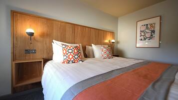 Una habitación de hotel con una cama grande, dos mesitas de noche, un cabecero de madera y dos lámparas fijadas a la pared.