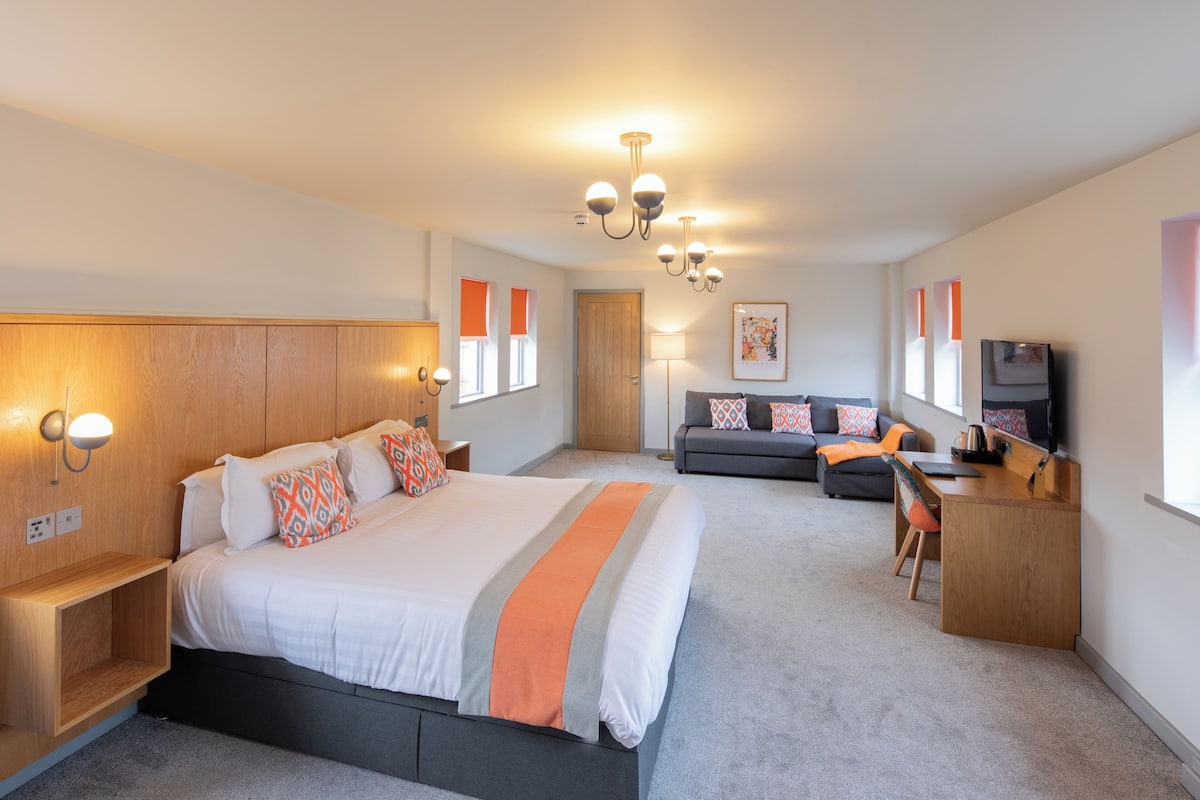 A modern hotel room with a large bed, a desk, a sofa, and a TV.
