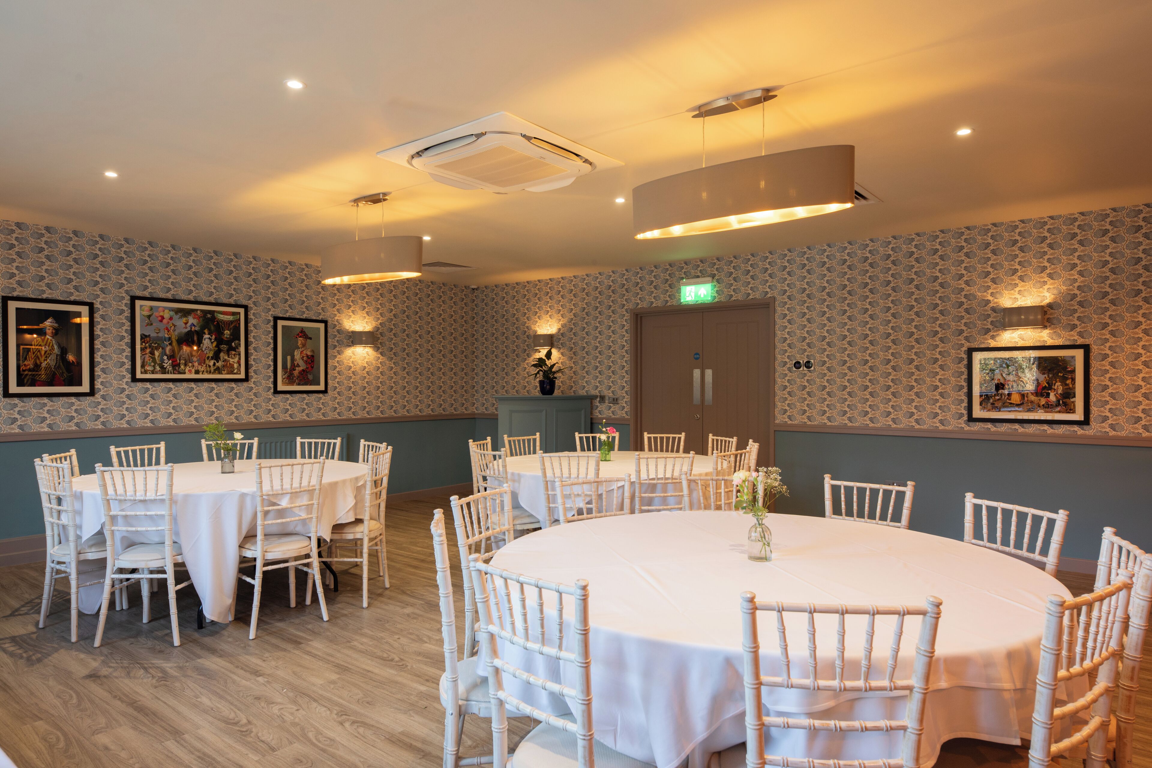 A dining area with round tables and white chairs, a wooden floor, and patterned wallpaper.